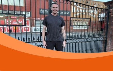 White man with brown hair stands in front of large black metal gates