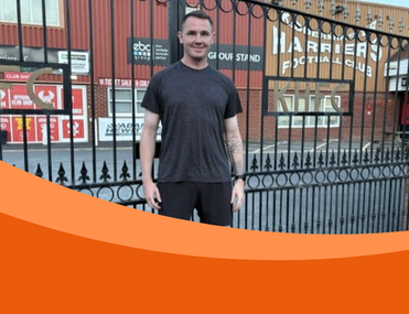 White man with brown hair stands in front of large black metal gates