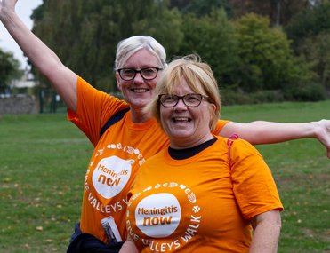 Two women in orange t-shirts looking towards the camera excitedly.