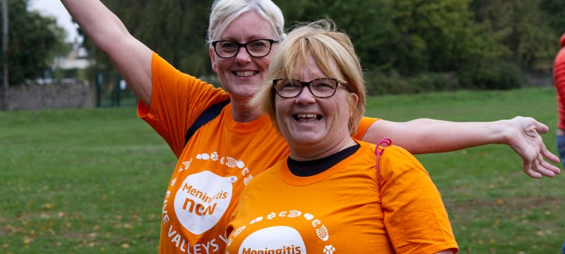 Two women in orange t-shirts looking towards the camera excitedly.