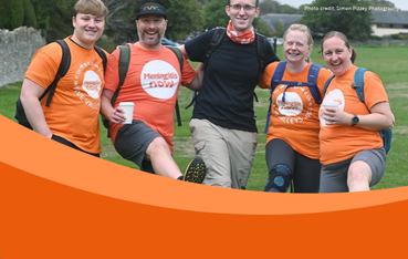 Group of walkers wearing orange Meningitis Now t-shirts smile and kick up their legs for the camera