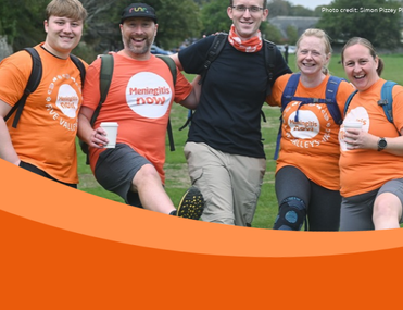Group of walkers wearing orange Meningitis Now t-shirts smile and kick up their legs for the camera