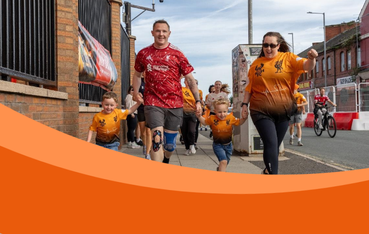 Family of mum and dad with two little boys run towards camera wearing orange shirts