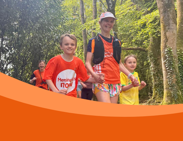 White woman in cap and running vest holds hands with two little boys with a background of trees