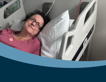 white woman with dark hair who's wearing glasses and a pink top lies in a hospital bed with her eyes open