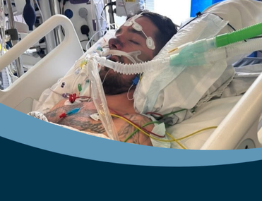 Young man with tattoos lies in hospital bed attached to tubes