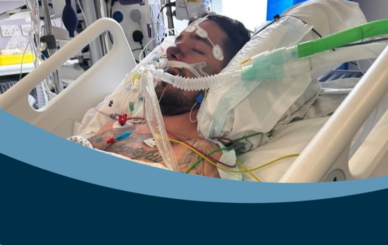 Young man with tattoos lies in hospital bed attached to tubes