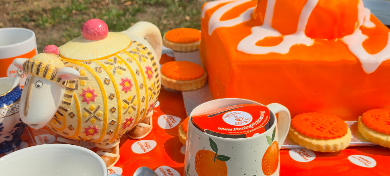 A garden table of orange themed baked goods with decorations and a collection of money for Meningitis Now