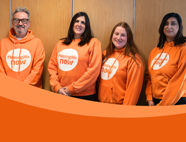 Four people stand in front of wooden wall wearing orange Meningitis Now hoodies