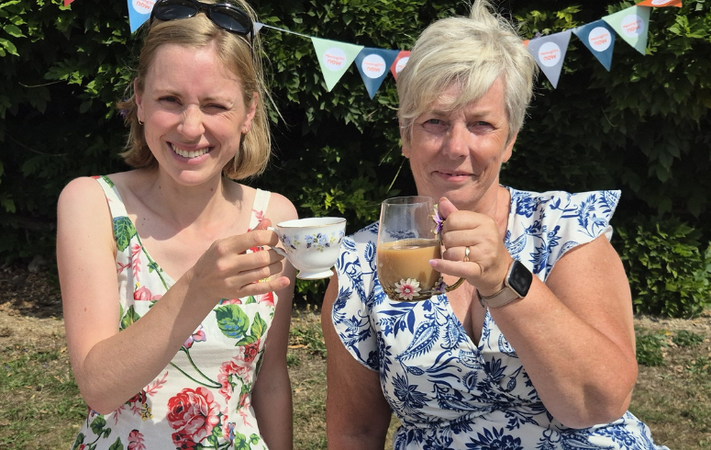 Two people in formal outfits sat at a garden party table cheersing drinks
