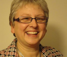 A smiling woman with short hair wearing a patterned blazer and glasses