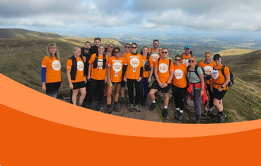 Large team of hikers wearing orange t-shirts pose in front of impressive landscape view