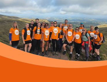 Large team of hikers wearing orange t-shirts pose in front of impressive landscape view