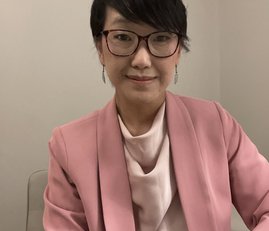 A woman wearing smart clothing and glasses looking at the camera