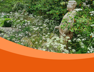 British garden in summer with wooden statue of young man facing away from camera