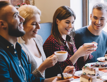 A group of adults at a cafe table having tea and chatting. The atmosphere is warm and engaging.