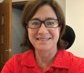A woman wearing a red shirt and black glasses sits on an office chair.