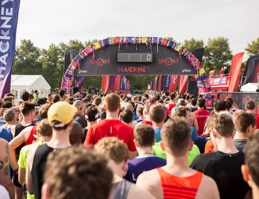 A group of runners in vests about to start the race under a arch and a banner for the Hackney Half marathon.