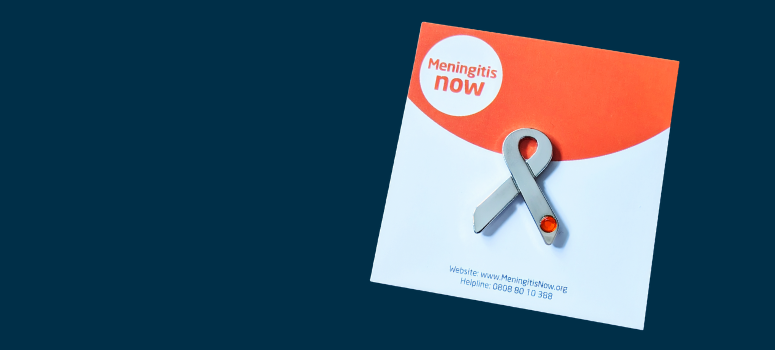 A silver ribbon badge backed onto card for Meningitis Now on a navy background