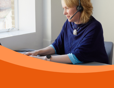 White woman with blonde hair looks away from camera to laptop screen. She is wearing a navy top and a headset.