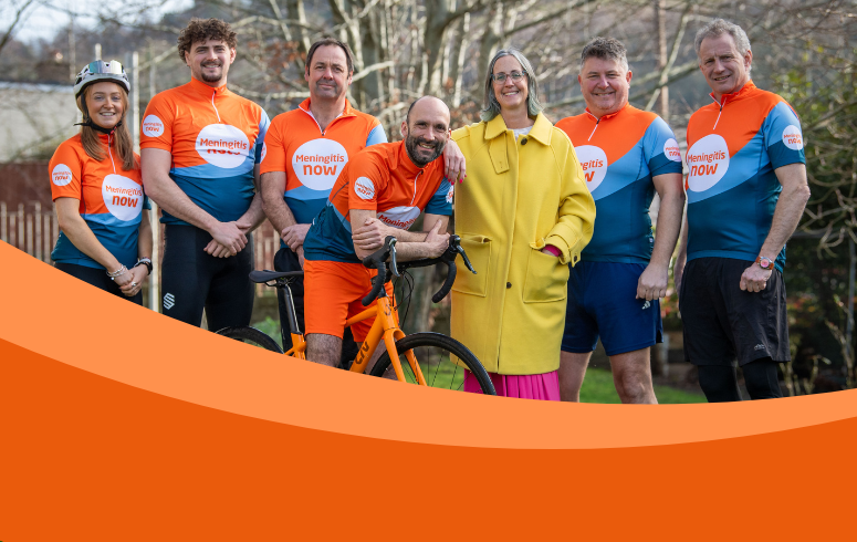 Group of seven white people in Meningitis Now sports vest smile at camera. CEO Tom Nutt is in the middle of the group on a bike.