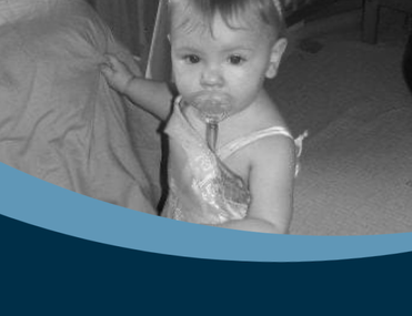 Black and white photo of a little white girl wearing a dress and sucking a dummy
