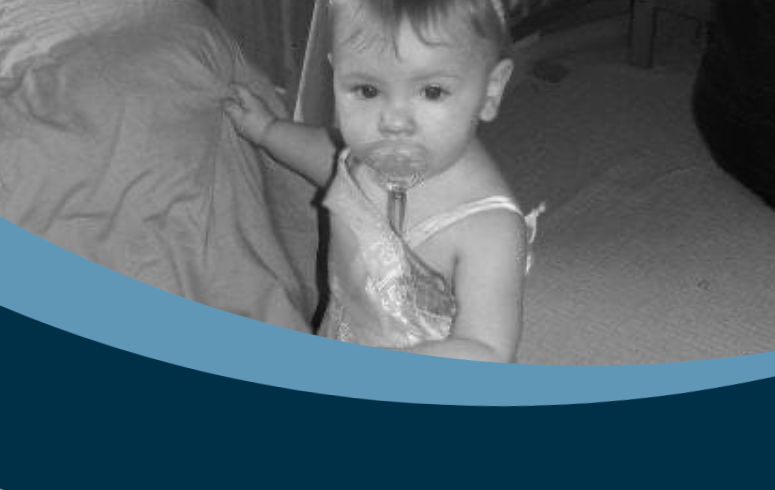 Black and white photo of a little white girl wearing a dress and sucking a dummy