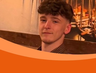 Portrait of a young man with curly brown hair in a restaurant, looking calmly at the camera; an orange curved graphic covers the lower frame.