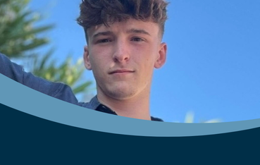 Young white man with brown hair looks at camera in front of a sky blue backdrop