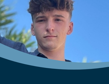 Young white man with brown hair looks at camera in front of a sky blue backdrop