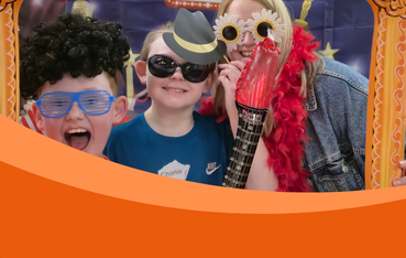 Two children and an adult dressed in funny costumes look through inflatable frame