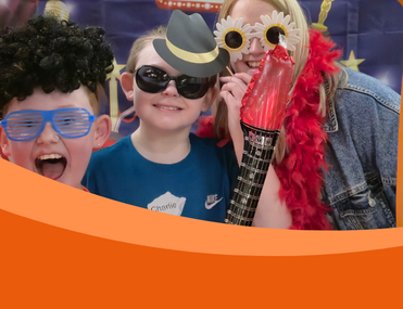 Two children and an adult dressed in funny costumes look through inflatable frame