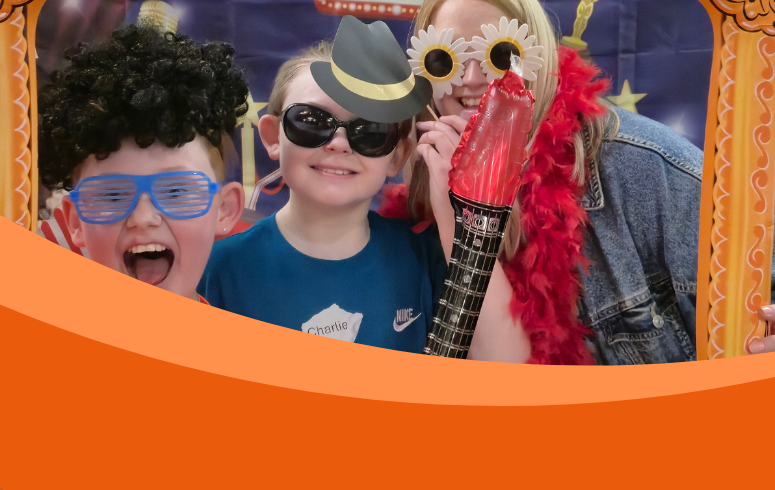 Two children and an adult dressed in funny costumes look through inflatable frame