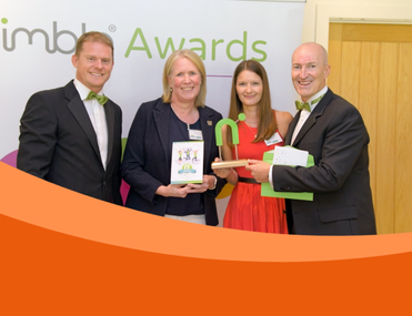 Four white people in smart clothes smile at camera holding green award statue in the shape of a letter 'N'