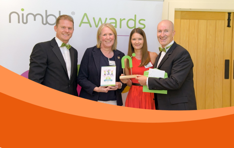 Four white people in smart clothes smile at camera holding green award statue in the shape of a letter 'N'