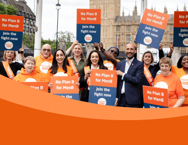 A group of individuals in orange t-shirts and sashes holding placards outside of government buildings that say 'No Plan B for Men B, Join the fight now' with a Meningitis Now logo at the bottom.