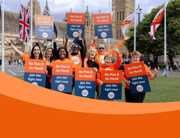 A group of individuals holding "No Plan B for MenB" signs stand together in front of the UK Parliament building. Flags are visible in the background.