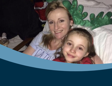 White woman with blonde hair in hospital bed cuddling young daughter with brown hair with Christmas decorations