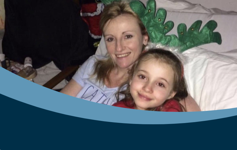 White woman with blonde hair in hospital bed cuddling young daughter with brown hair with Christmas decorations