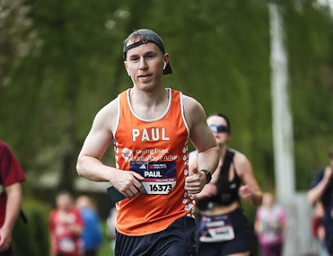 A man running in an event wearing a Meningitis Now vest and hat.