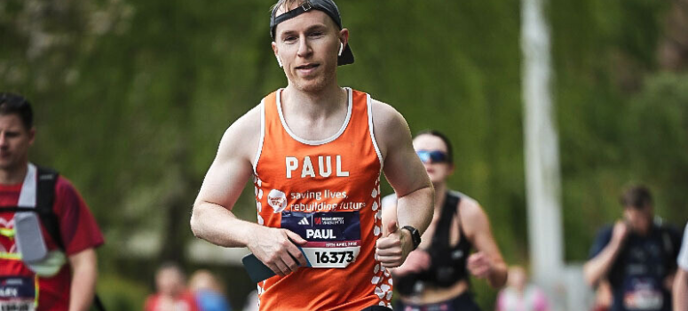 A man running in an event wearing a Meningitis Now vest and hat.