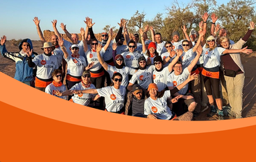Large group of people, many wearing sunglasses and t-shirts look at the camera, some with arms above their heads