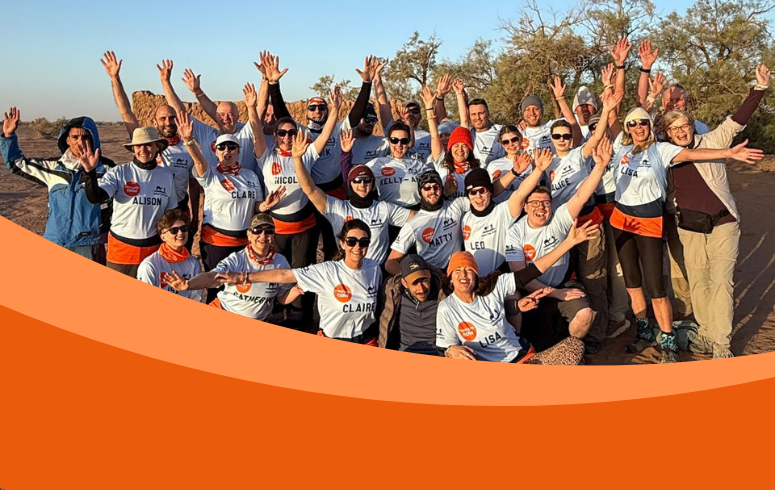 Large group of people, many wearing sunglasses and t-shirts look at the camera, some with arms above their heads