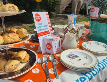 A table in the garden of orange themed baked goods with decorations and a collection of money for Meningitis Now