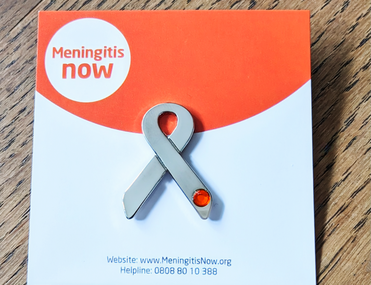 A silver ribbon badge backed onto card for Meningitis Now