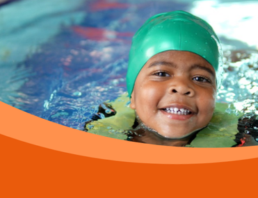 Black child wearing green swim cap smiles whilst swimming