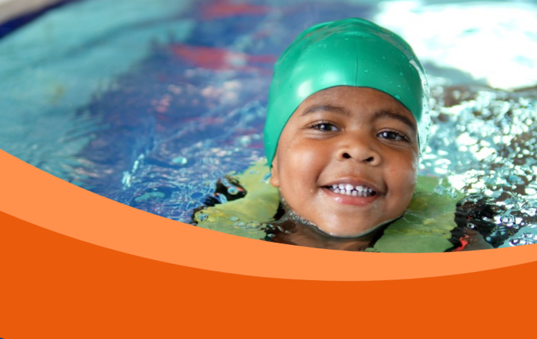 Black child wearing green swim cap smiles whilst swimming