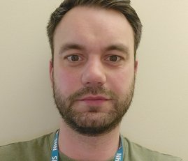 A man with a beard wearing a green jumper and a blue lanyard.